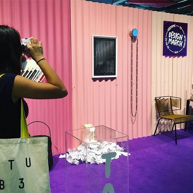 A room with pink walls made from corrugated metal and purple floor. Dark-haired woman taking a picture. 