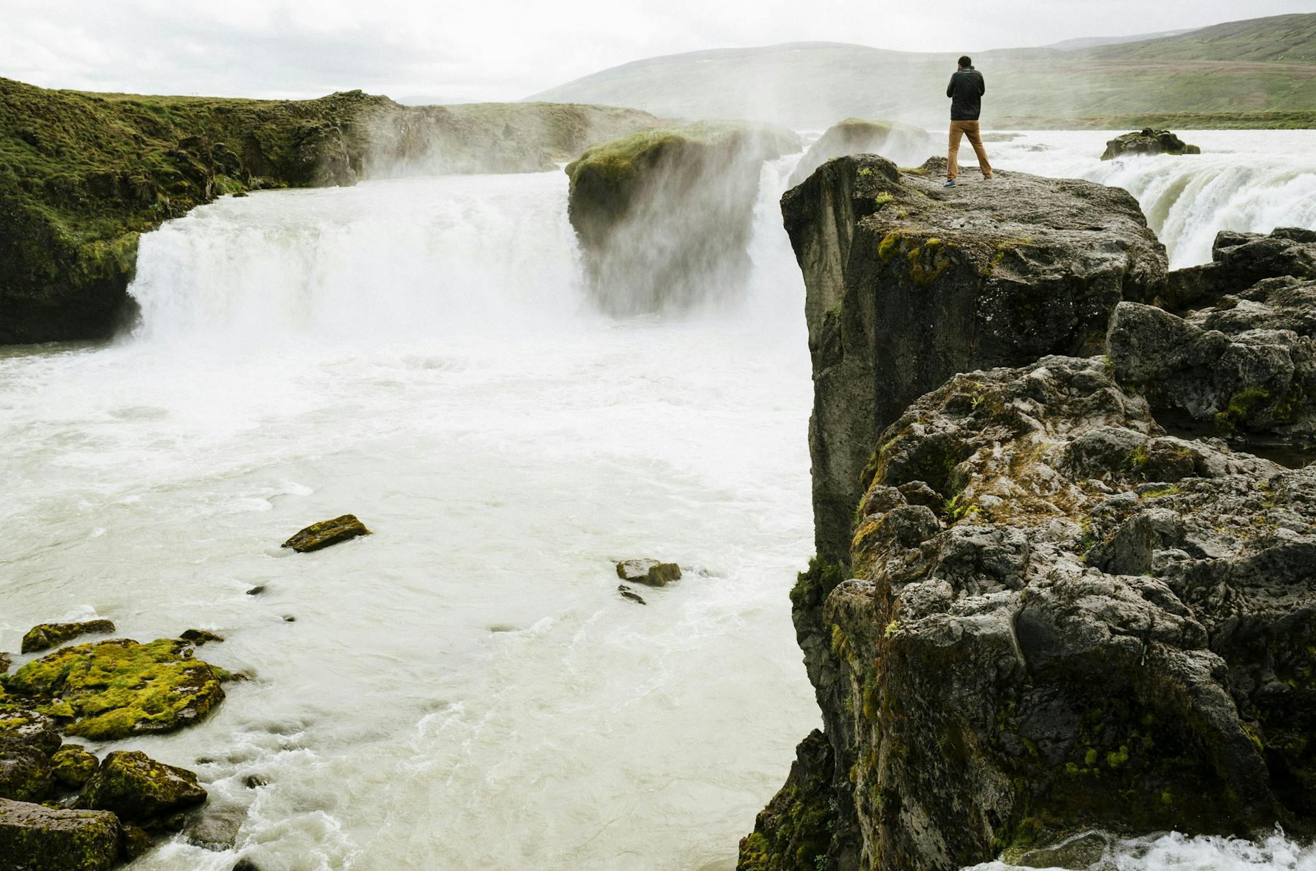 A man on the edge of a cliff, near a waterfall in Iceland. 