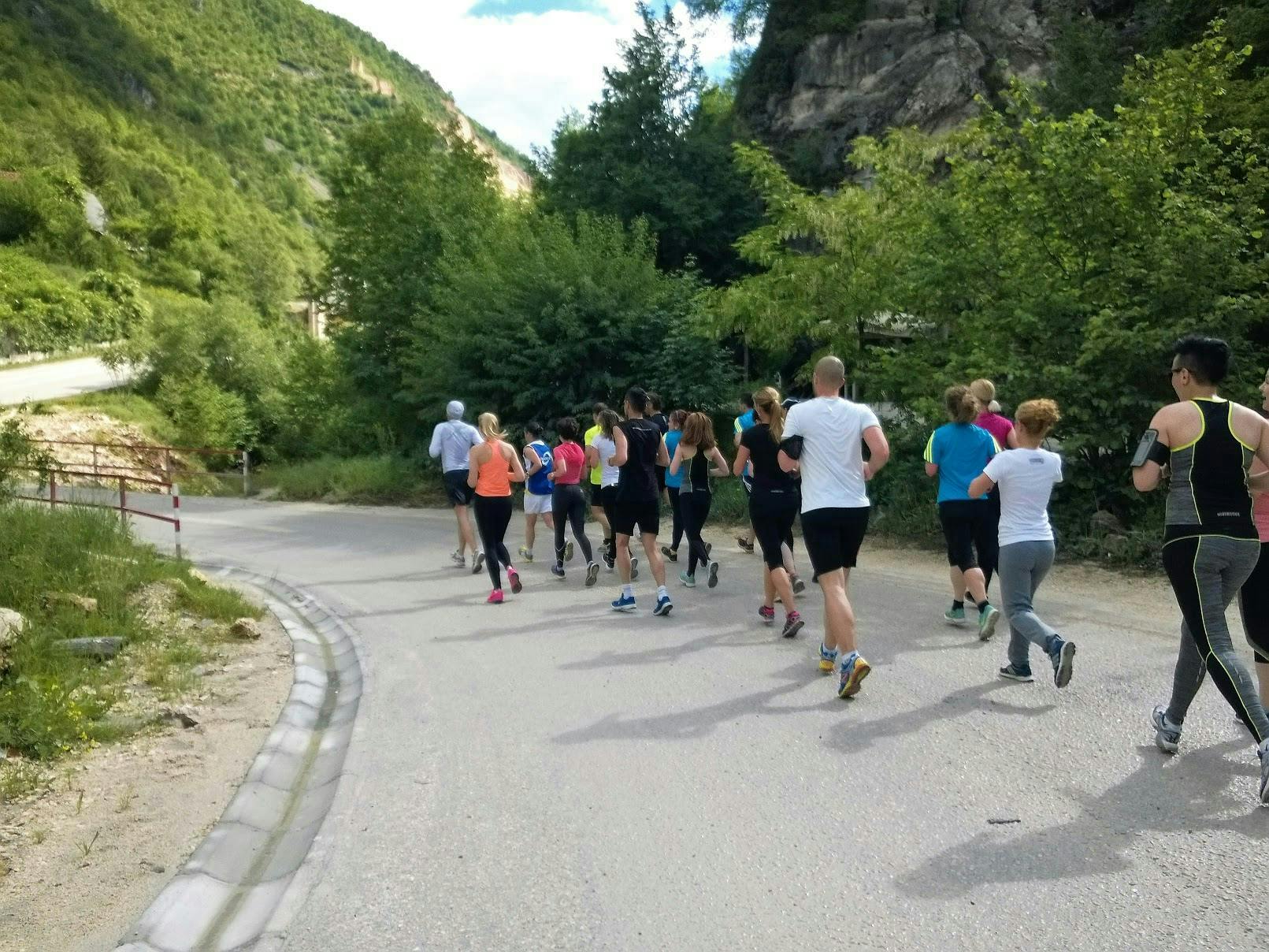 A group of runners running up a green hill. 