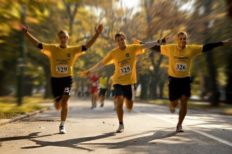Three runners in yellow shirts waiving at the camera while running. 