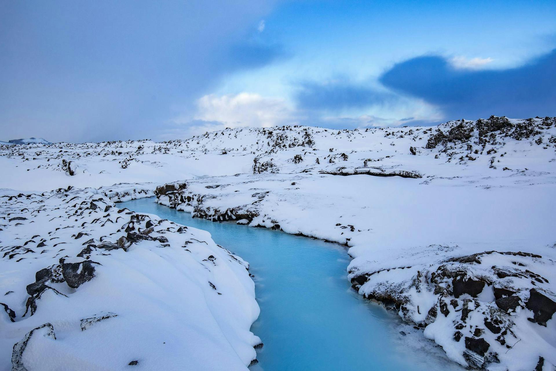 Snow and lava surrounding a river of blue geothermal water. 
