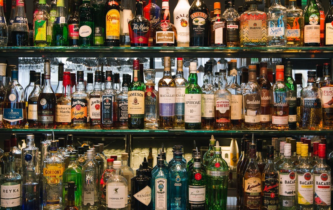 A huge selection of liqueurs stacked on glass shelves. 