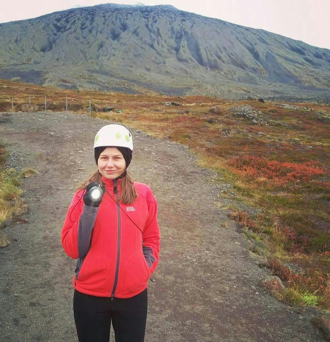 A woman in a white helmet wearing a red sweater in front of a mountain near Vatnshellir cave, Snæfellsnes Peninsula. 
