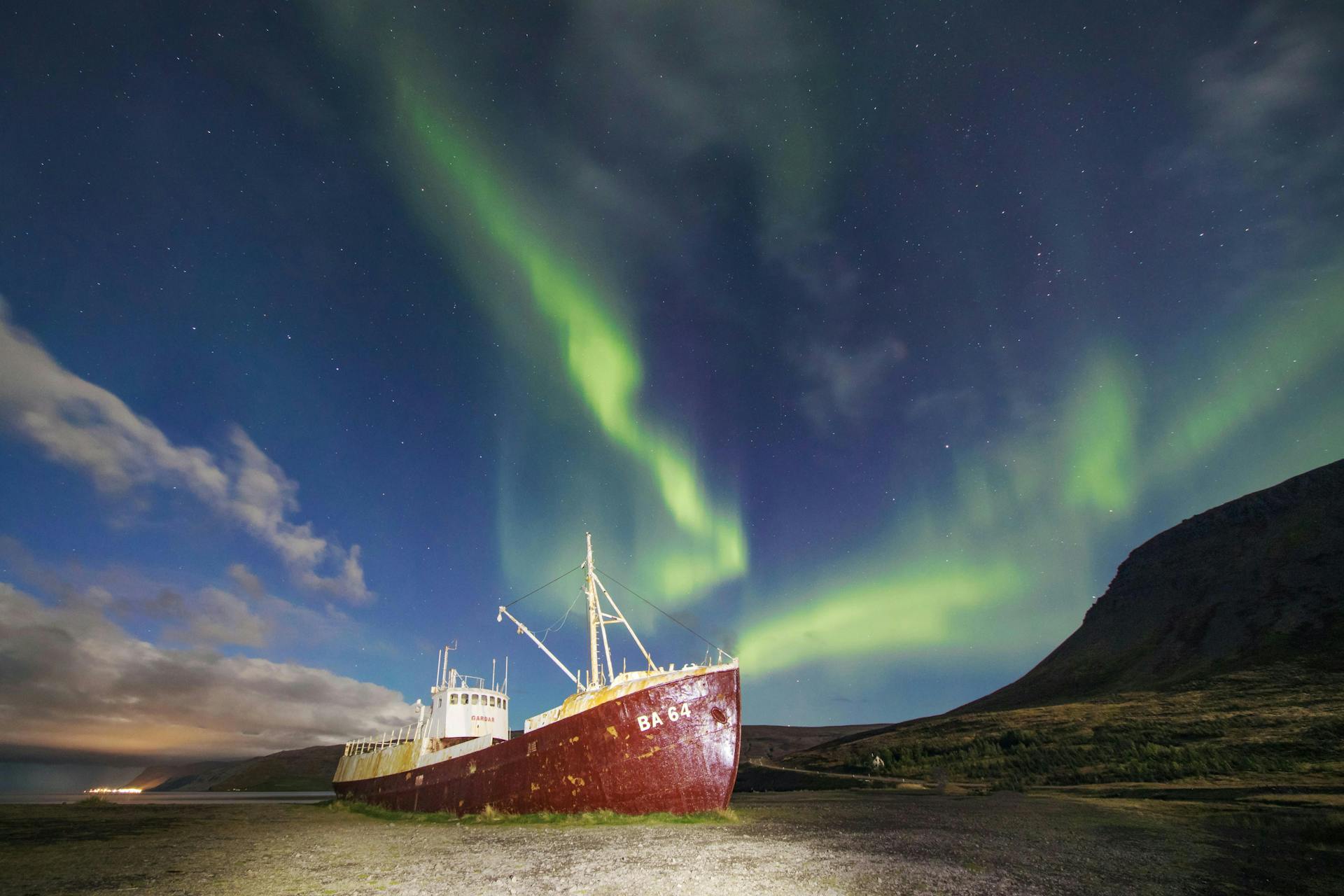 A shipwreck on a beach, northern lights dancing in the sky above. In the southern part of the Westfjords, Iceland. 