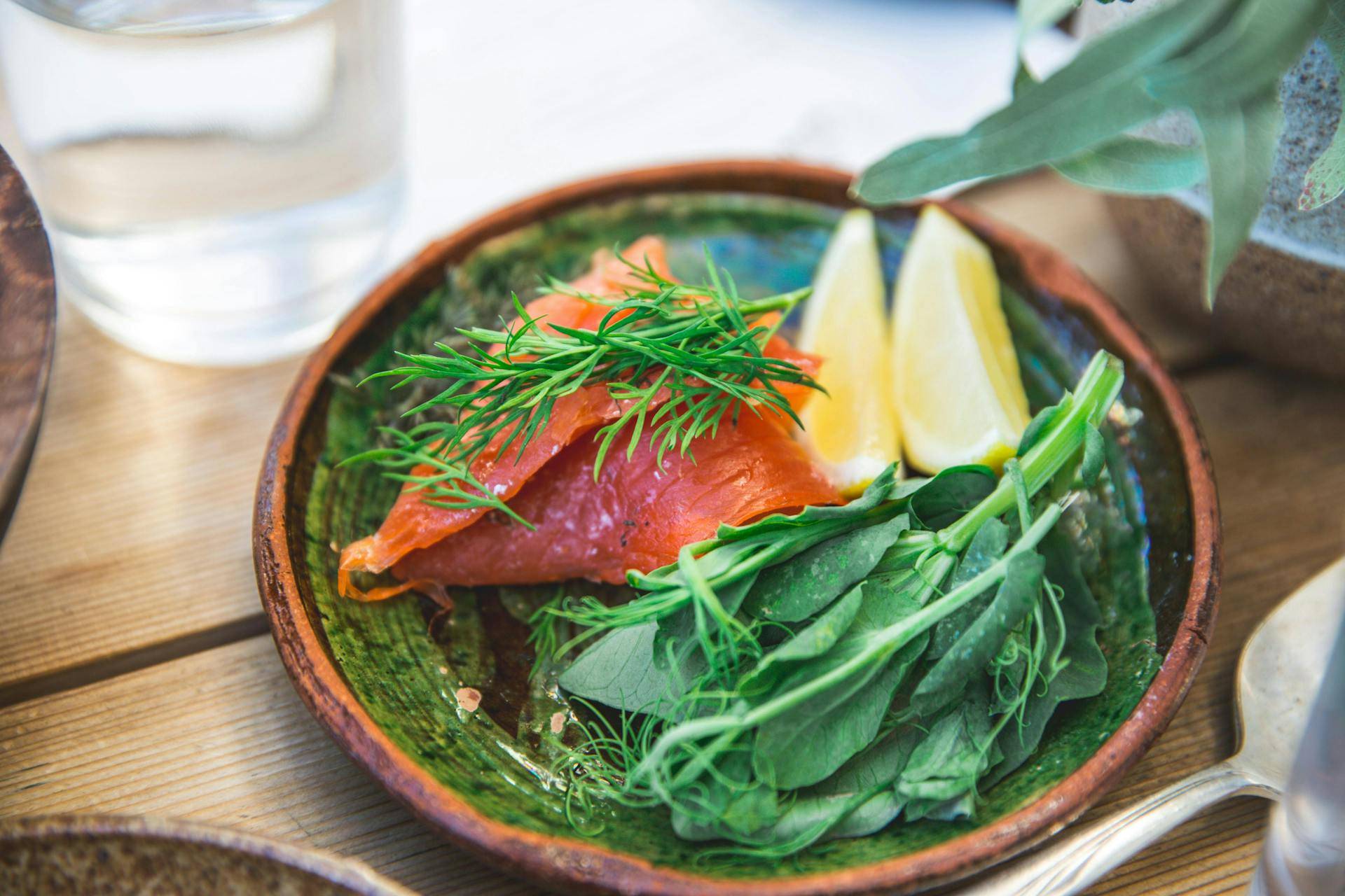 A plate with smoked salmon, spinach leaves and a slice of lemon. 