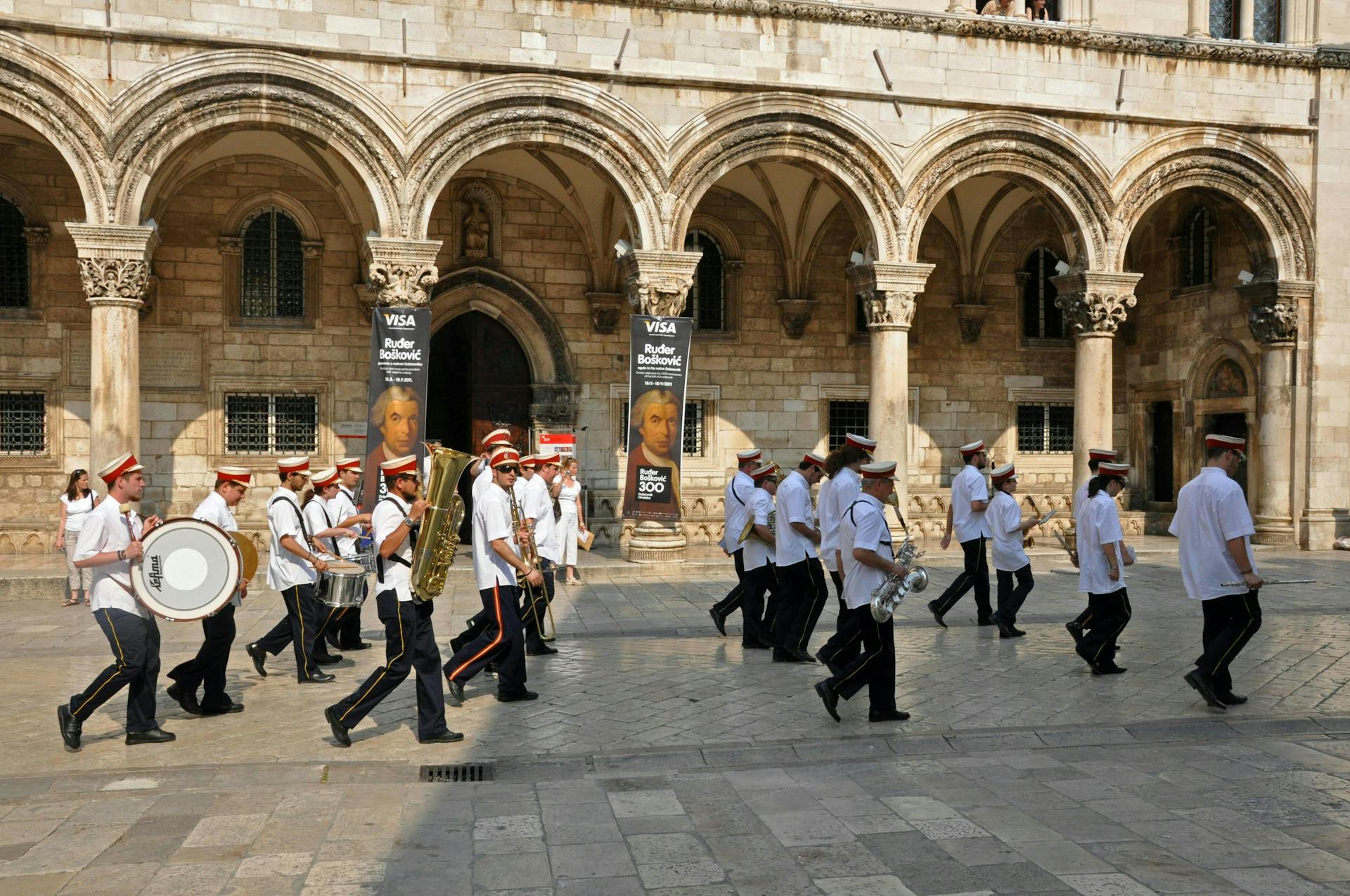 A brass band marching by a palace. 