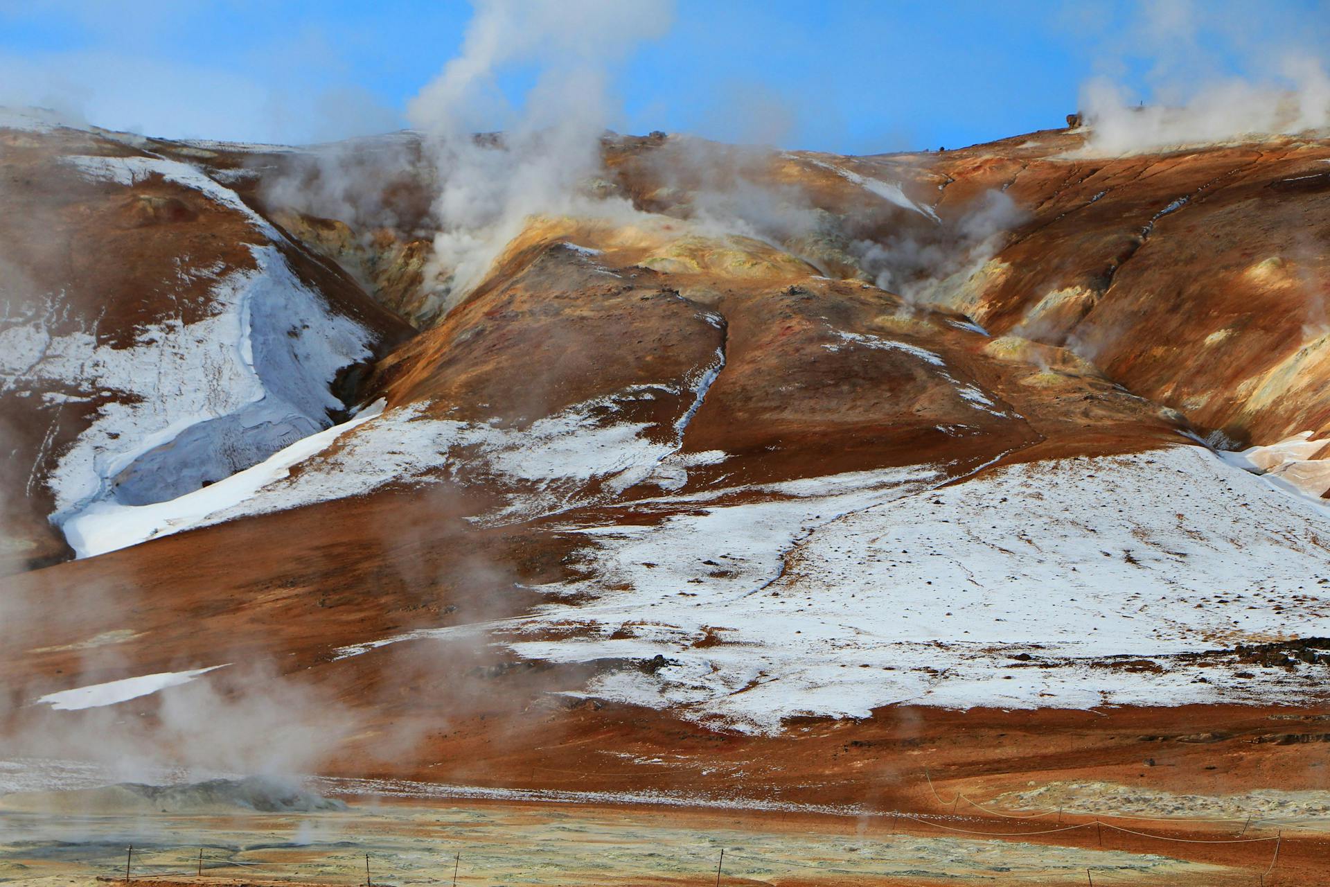 Geothermal area in Mývatn, characterised by columns of steam and reddish surface. 
