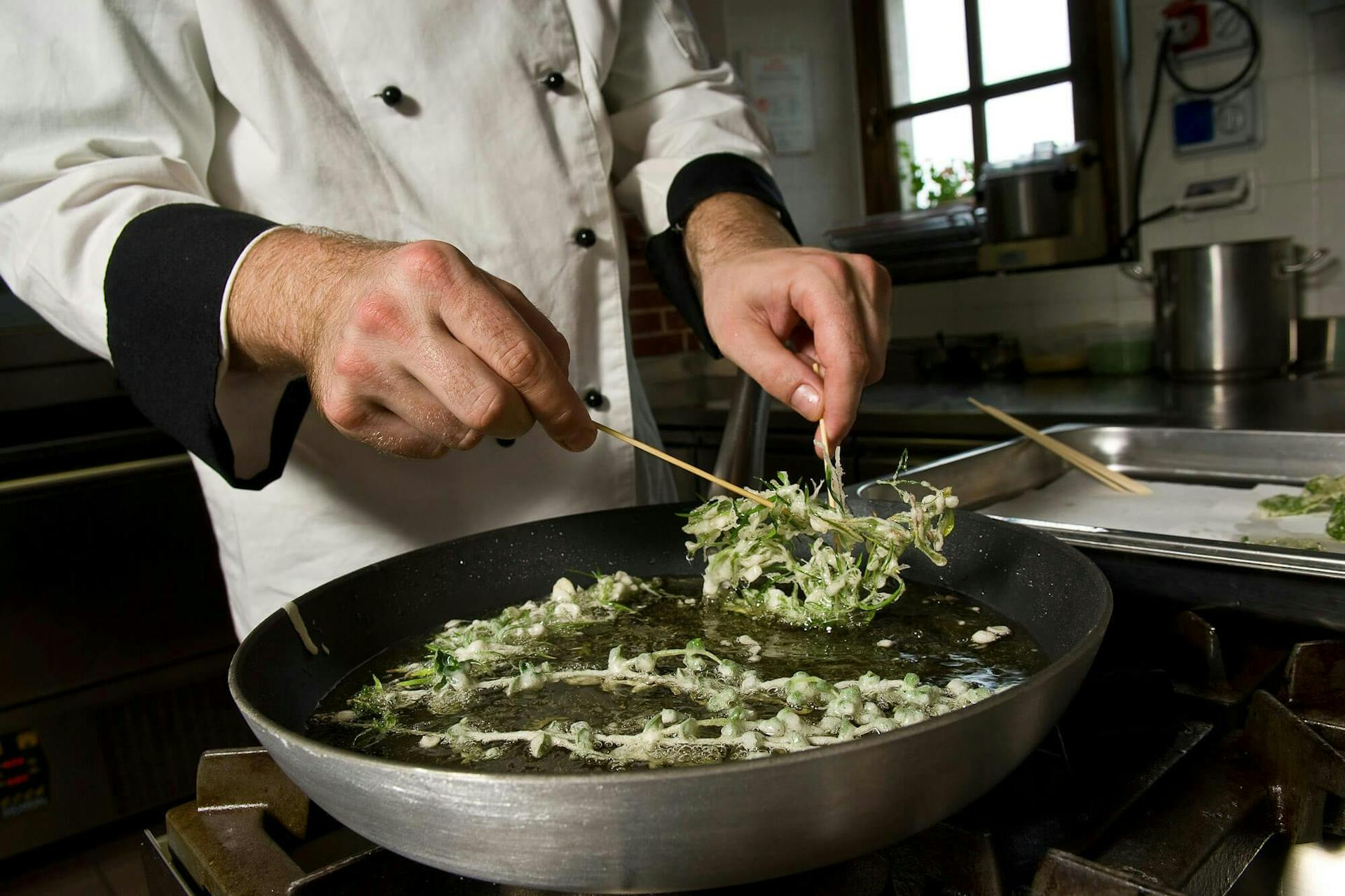 A man wearing chef's clothes frying herbs in a pan. 
