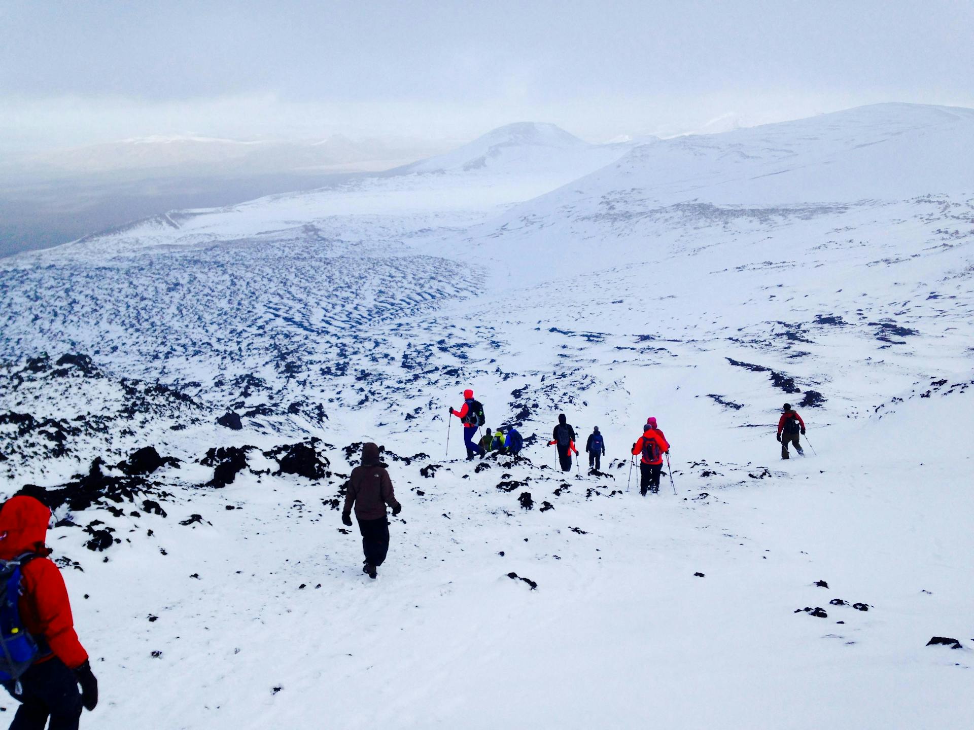 A dispersed group of hikers walking down the snowy hills of Mt. Hekla. 