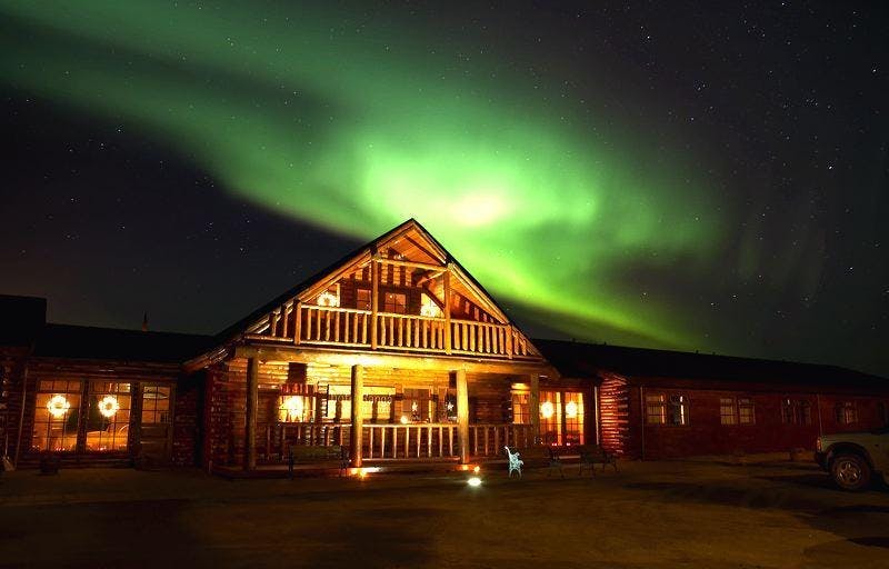 A cabin-style hotel, dark sky and bright green northern lights. 
