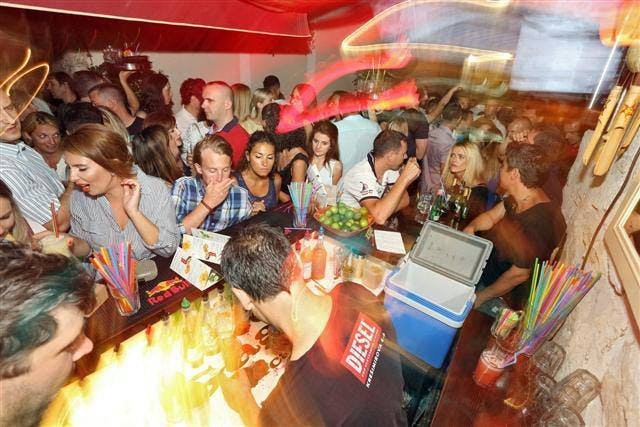 A crowd of people dancing while a waiter mixes cocktails. 