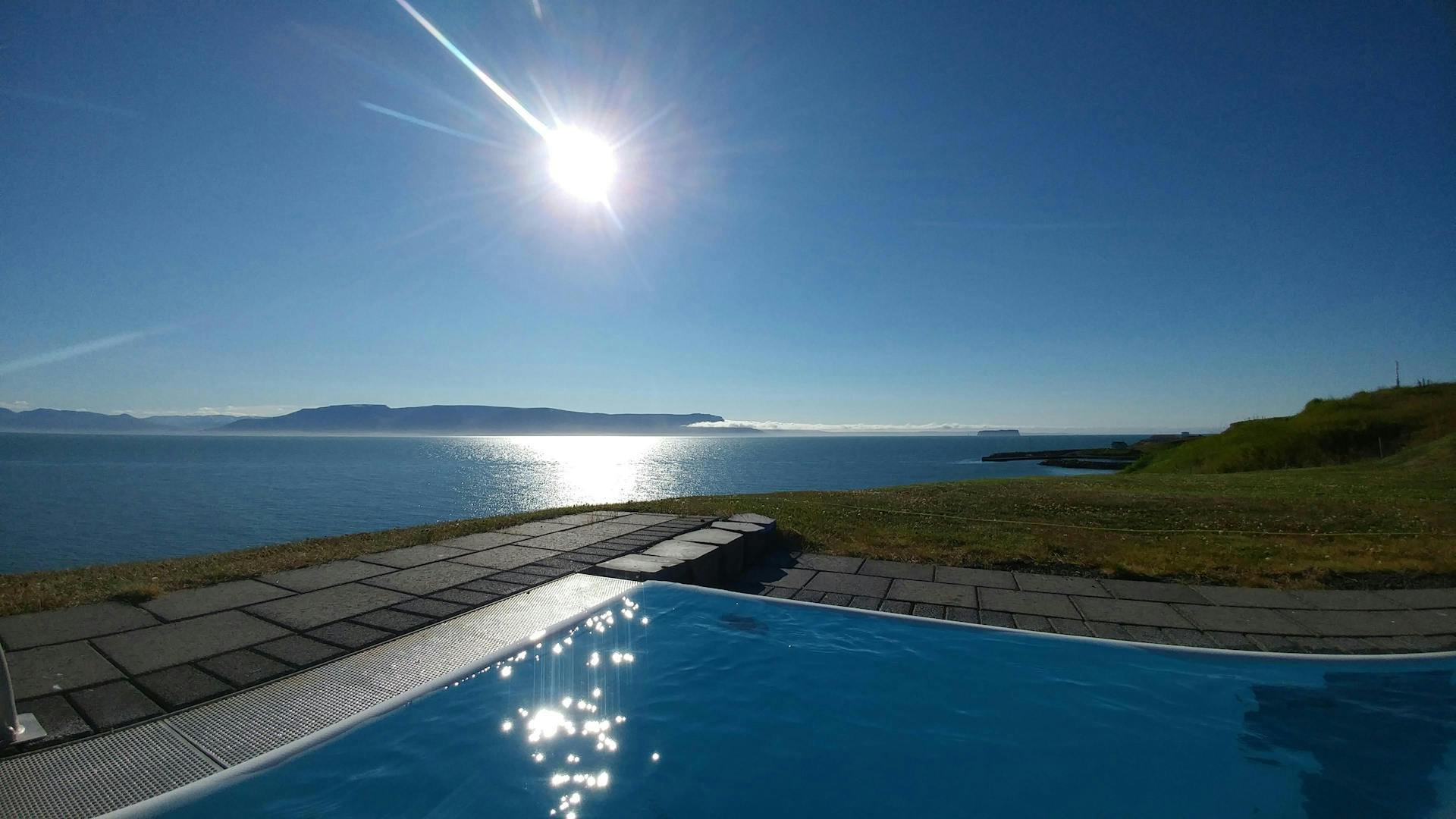 The ocean seen from a swimming pool, sun is shining above. 