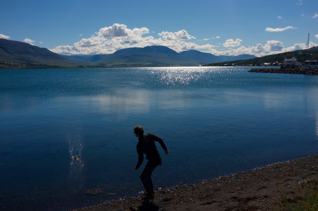 A man throwing a stone into a calm fjord. 