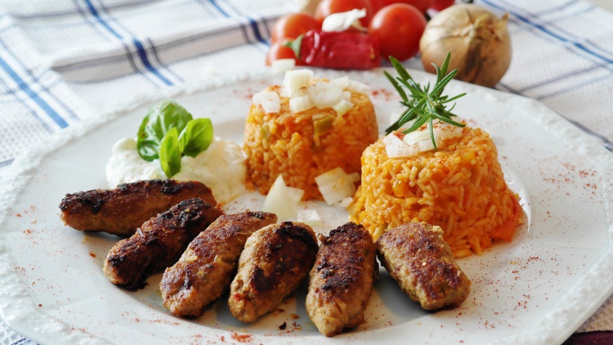 6 small sausages on a white plate with some rice. 