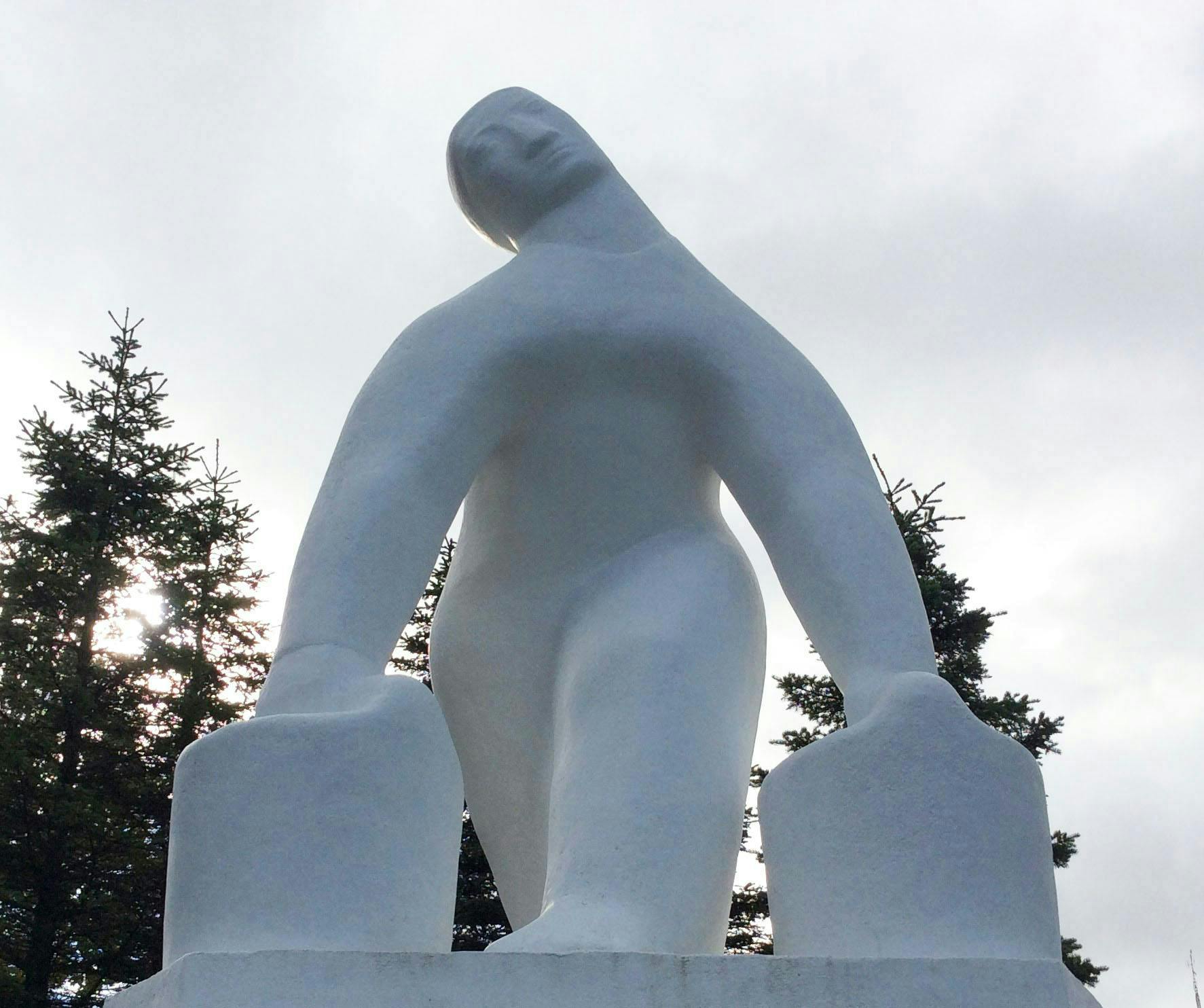 A white outdoor sculpture of a person carrying a bucket of water in each hand. 