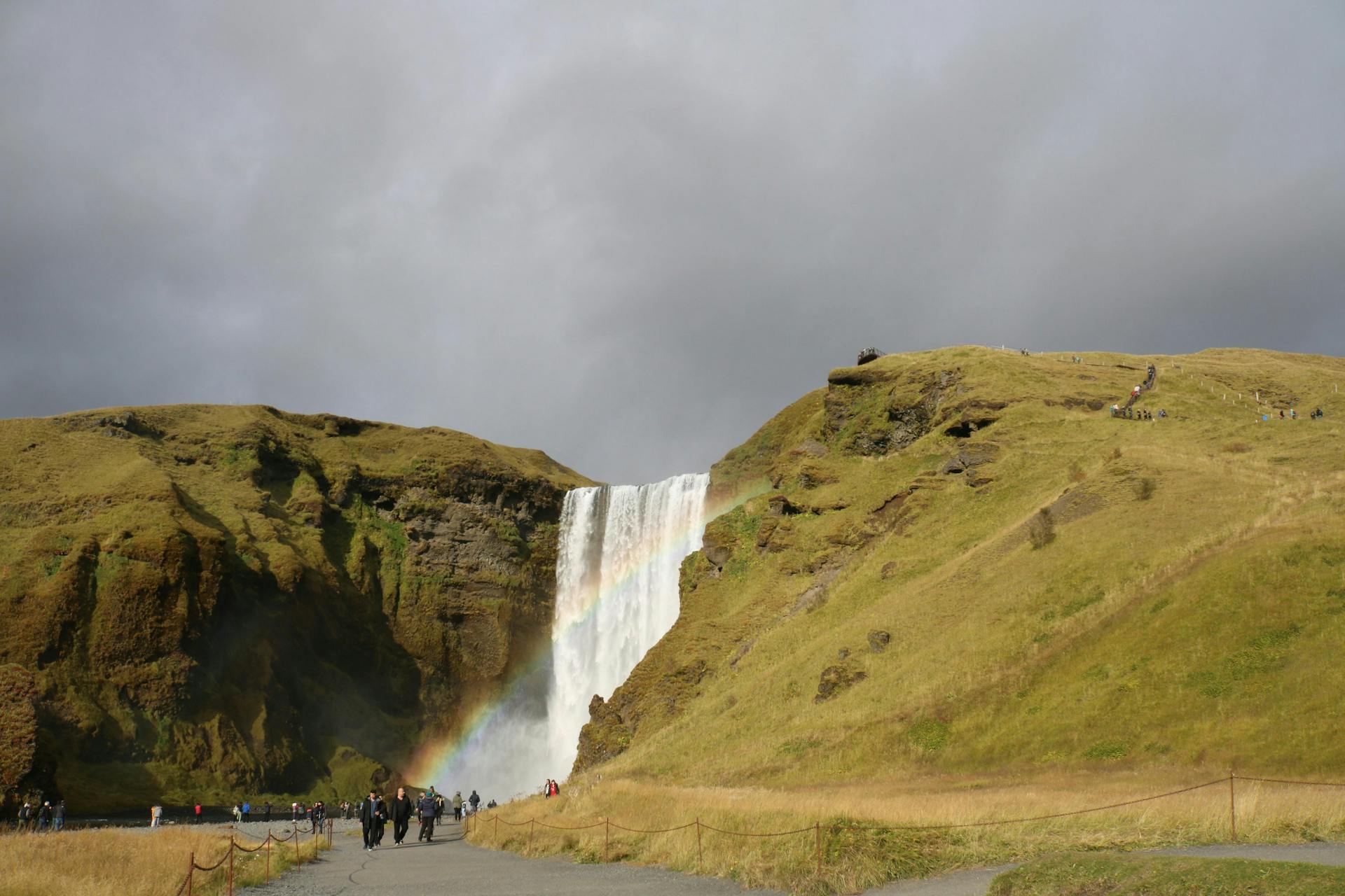 Skógafoss and people walking on the path leading towards it. 