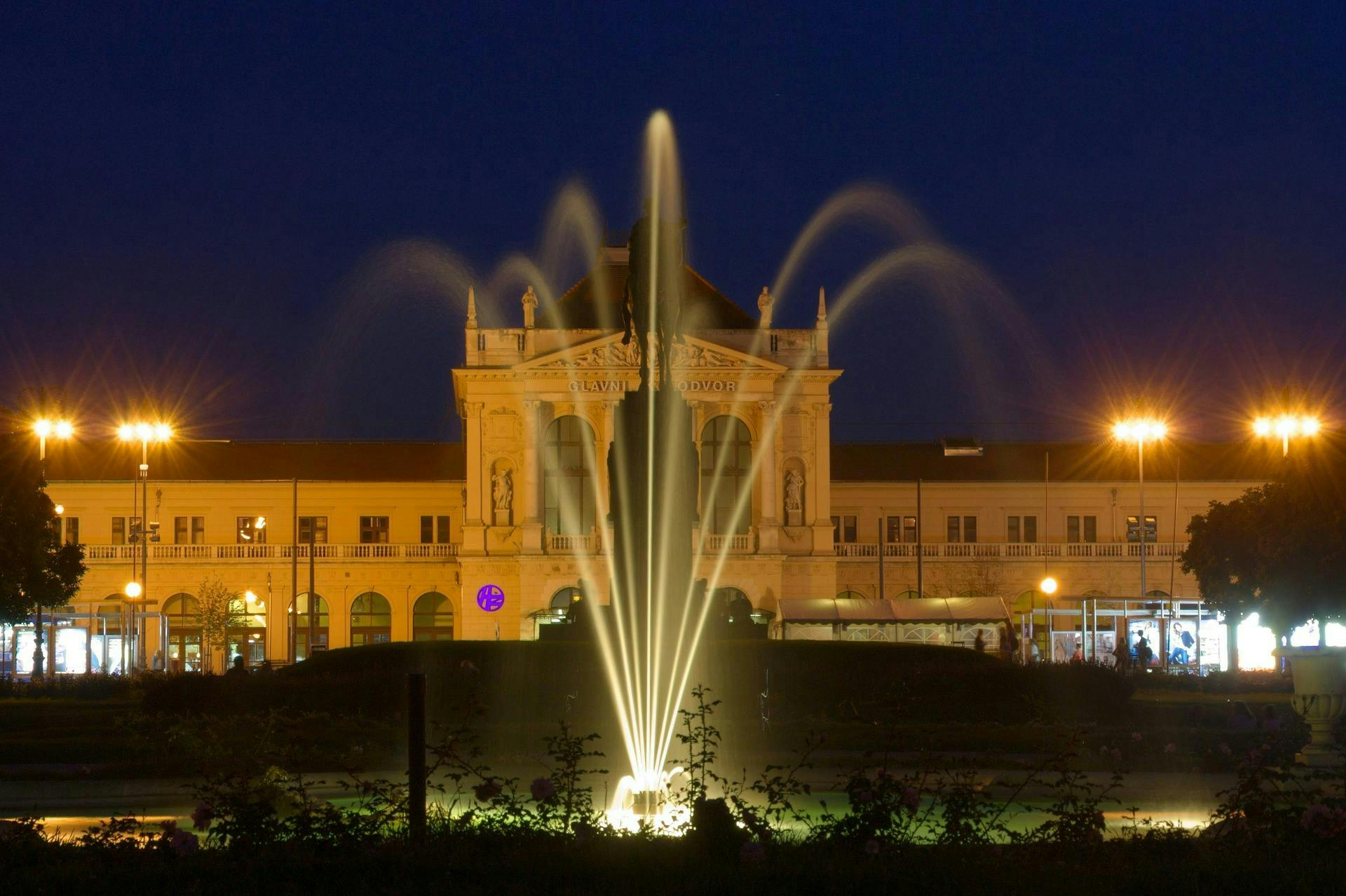 A water fountain in front of a majestic building, at night. 