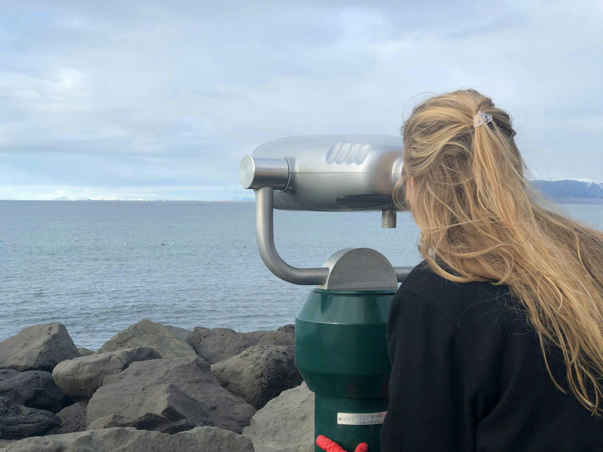 A girl looking through binoculars trying to spot whales at sea. 