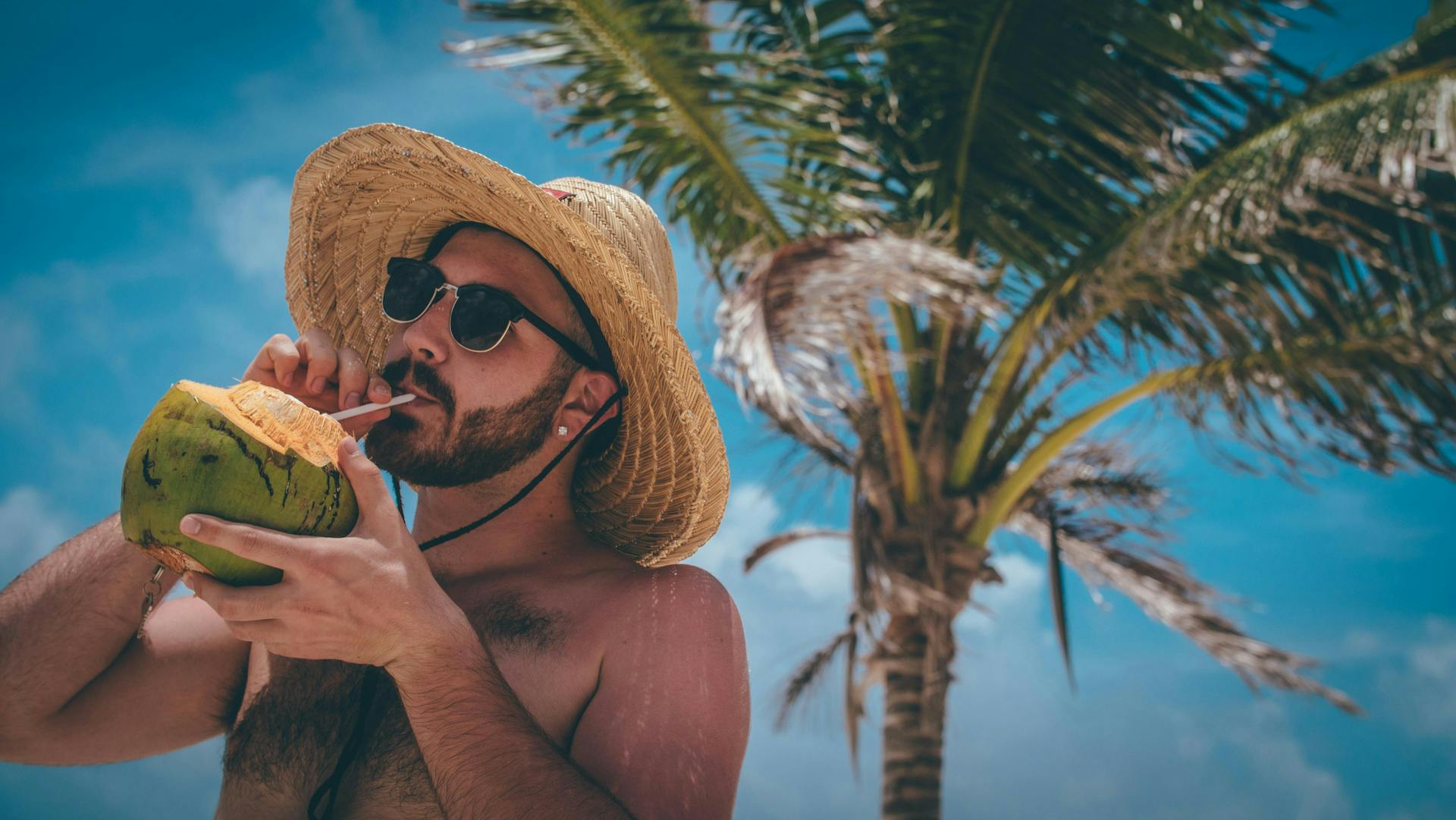A man drinking coconut water from a coconut on the beach. 