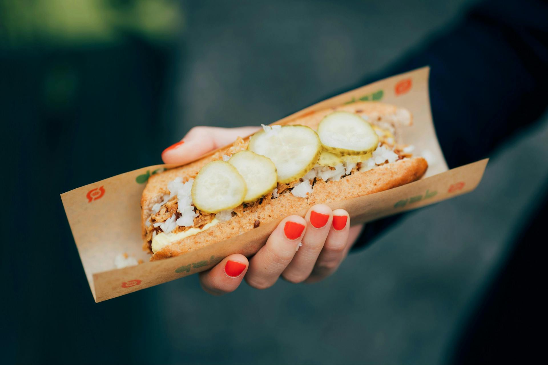 A woman's hand holding a hot dog with pickles. 