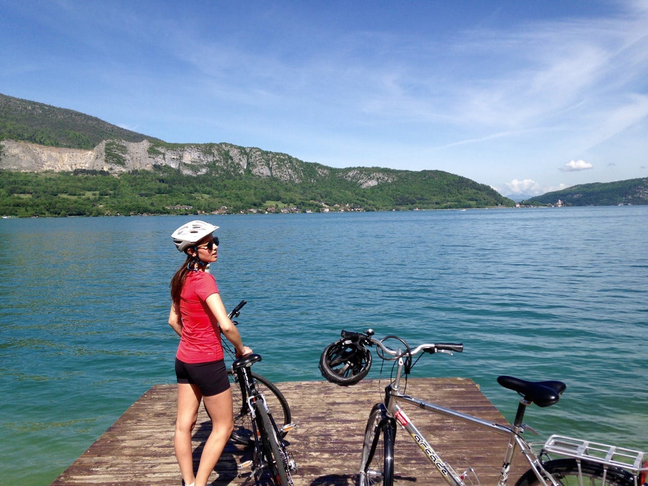 A woman with a bicycle helmet and two bikes on a dock by Lake Annecy, France. 