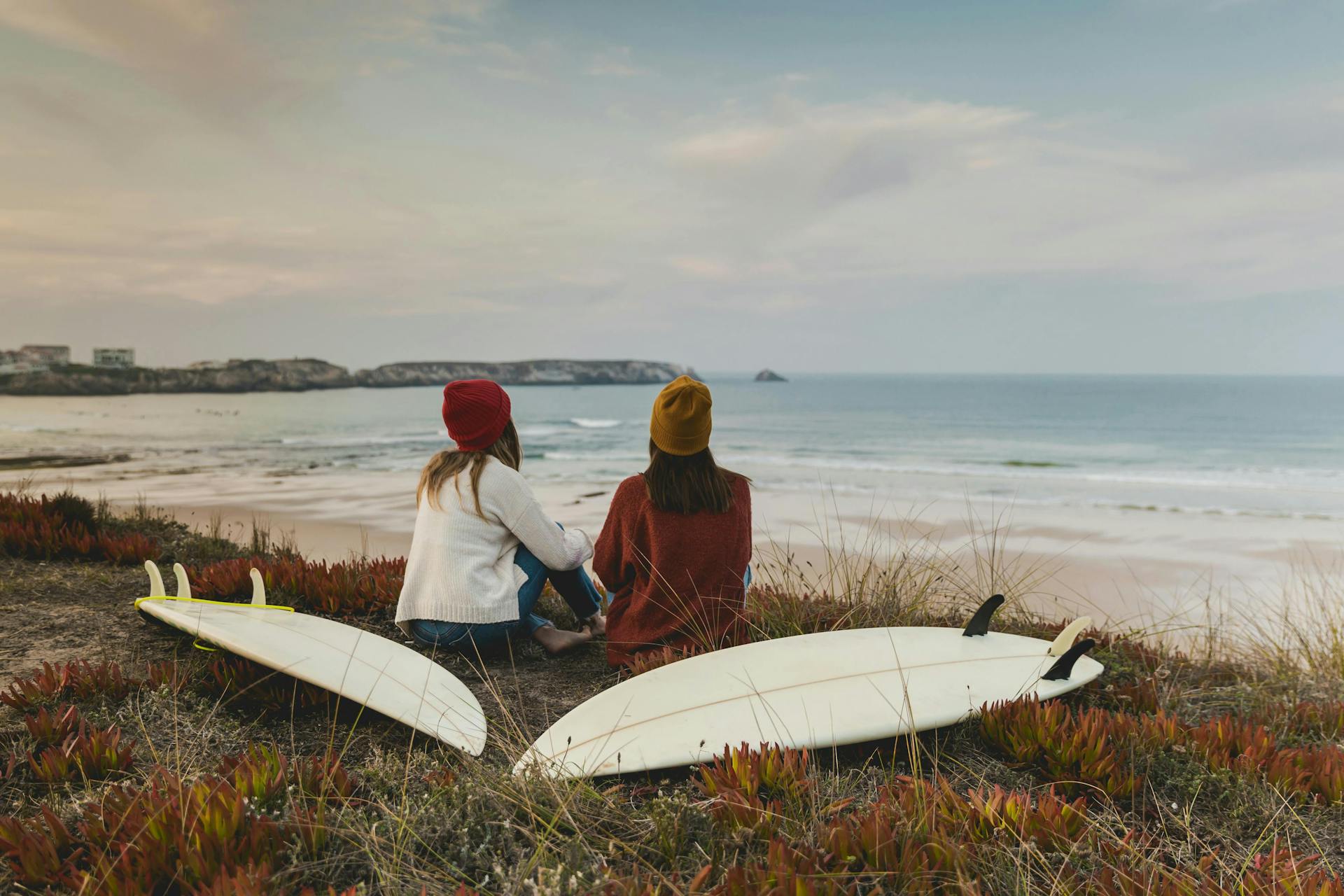 Two surfers sitting with there surf boards above a beach in Portugal. 